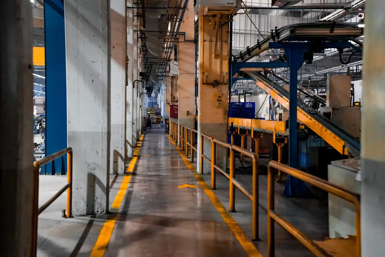 An empty walkway marked with yellow floor lines running between conveyor lines and machinery inside an industrial plant.